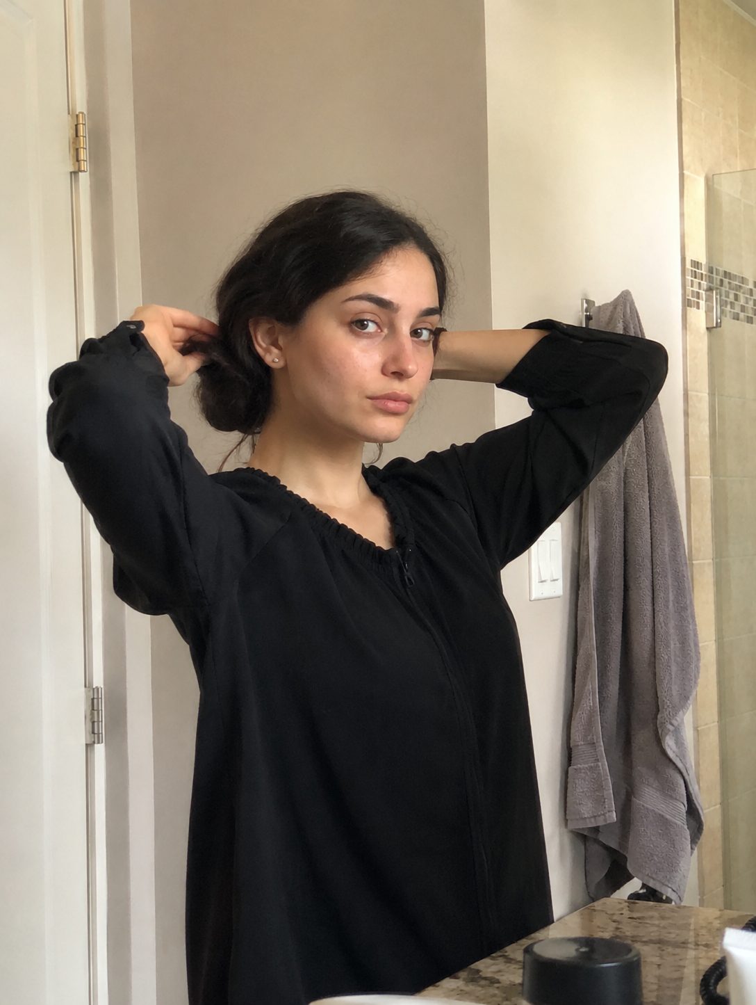 Gathering hair into a loose low bun before wrapping a hijab